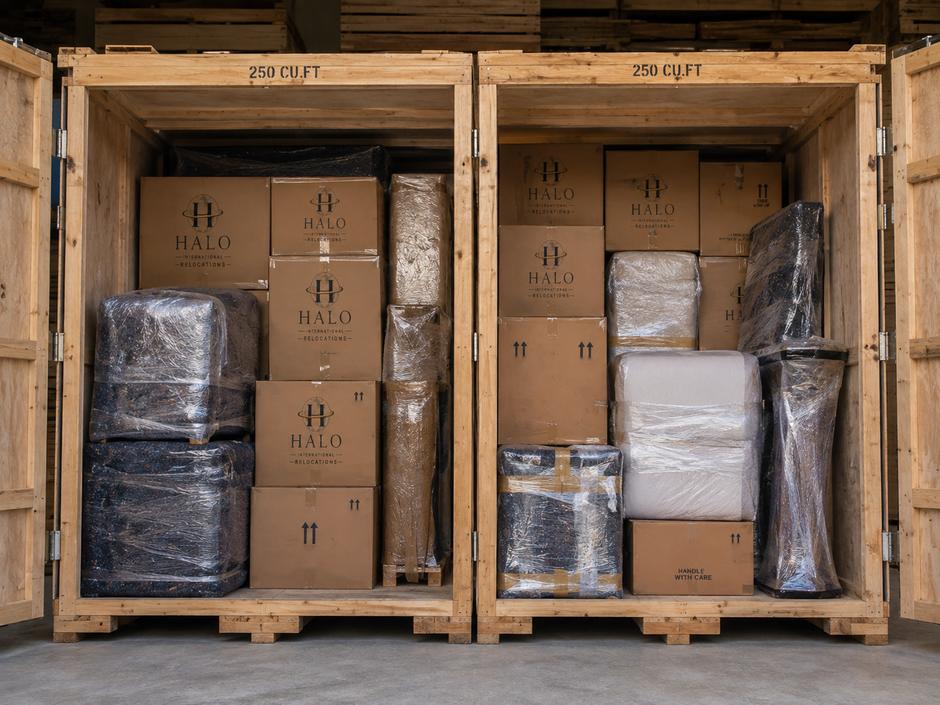 Two open wooden storage containers packed with Halo cartons and wrapped furniture, each stencilled 250 cubic feet